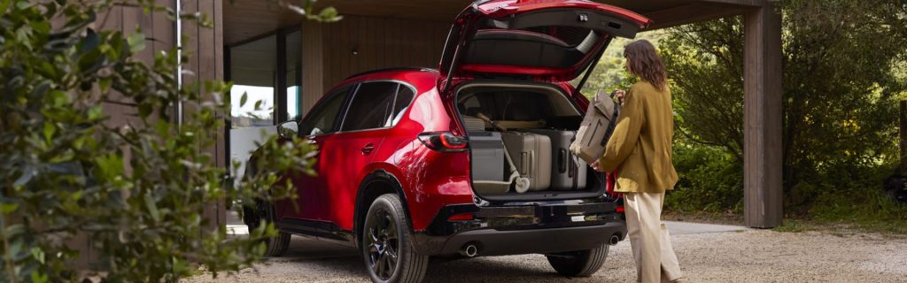 Red Mazda CX-5 SUV with its rear liftgate open as a person loads luggage outside a modern home.