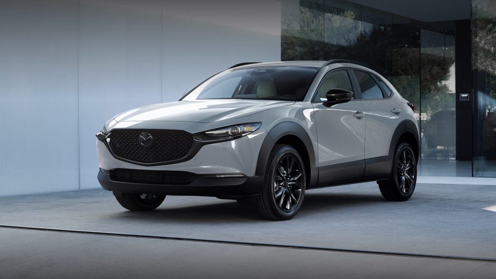 2026 Mazda CX-30 compact SUV in white parked outside a modern building, highlighting its sleek design and refined styling.